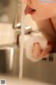 A woman is drinking water from a faucet in the kitchen.