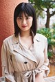 A woman in a beige trench coat leaning against a wall.