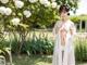 A woman in a white robe standing in a garden.