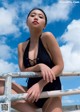 A woman in a black bathing suit sitting on a railing.