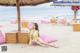 A woman in a yellow bikini sitting on a pink bean bag chair on the beach.